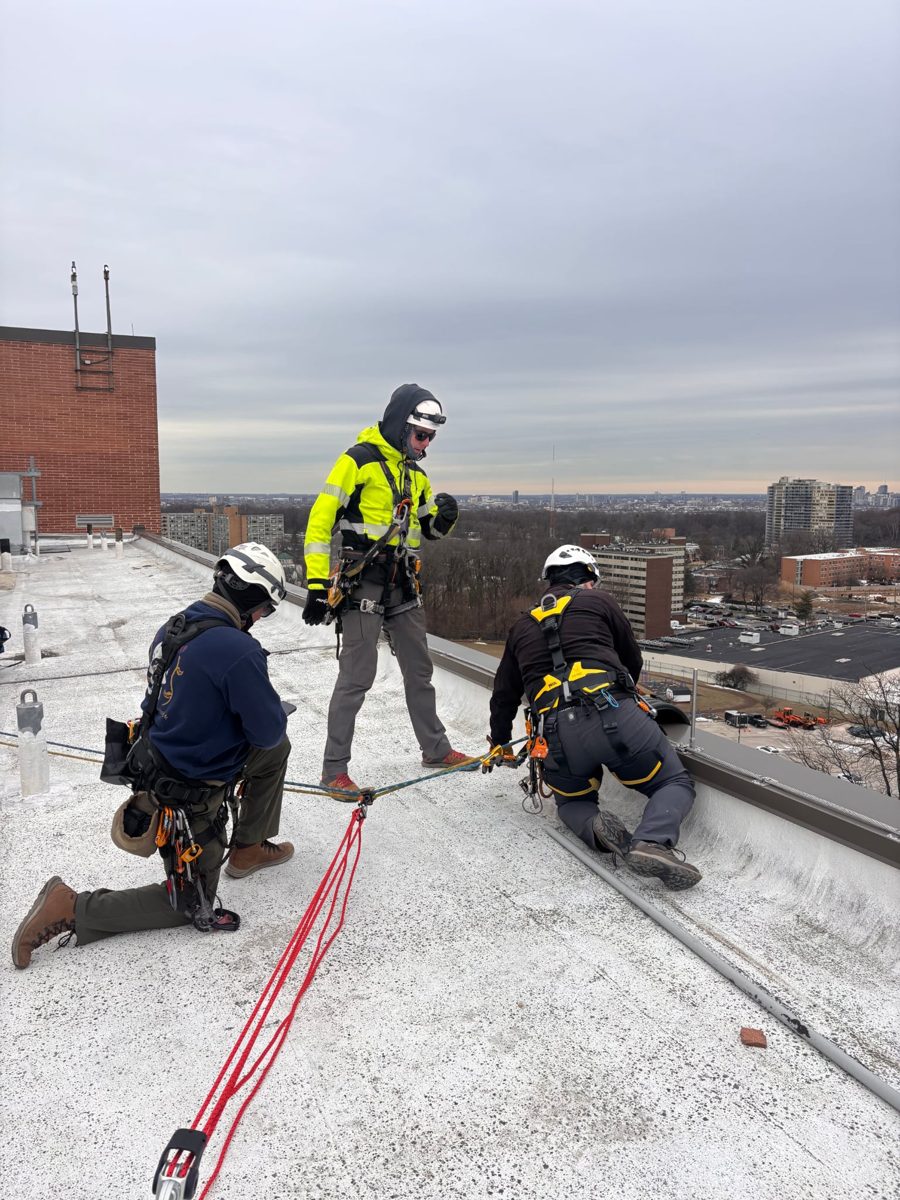 Three rope access technicians rigging an anchor line on a snowy rooftop